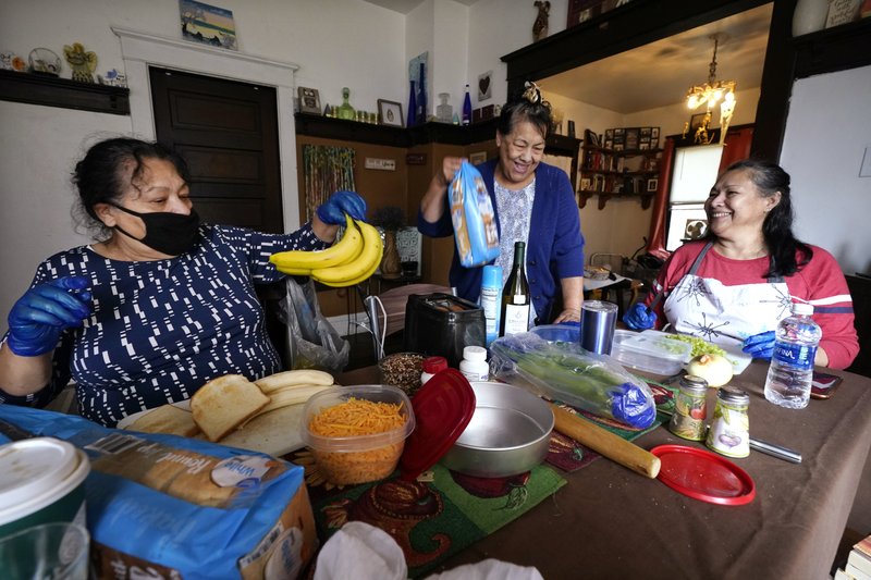 Olga Garcia, left, and her sisters Francis Garcia, center, and Anna Garcia work to prepare an afternoon family meal Wednesday, Nov. 4, 2020, in the family home in Sedro-Woolley, Wash. On any other Thanksgiving, dozens of Olga's family members would squeeze into her home for the holiday. But this year, she'll deliver food to family spread along 30 miles of the North Cascades Highway in Washington state. If the plan works, everyone will sit down to eat in their own homes at precisely 6:30 p.m. and join a group phone call. (AP Photo/Elaine Thompson)